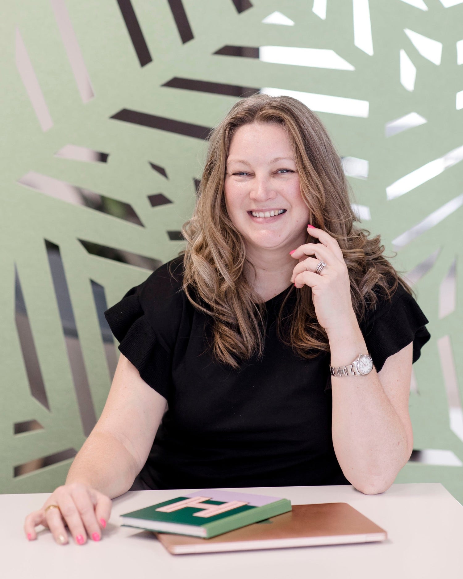 Woman sitting at a table with a green and brown book against a decorative wall.