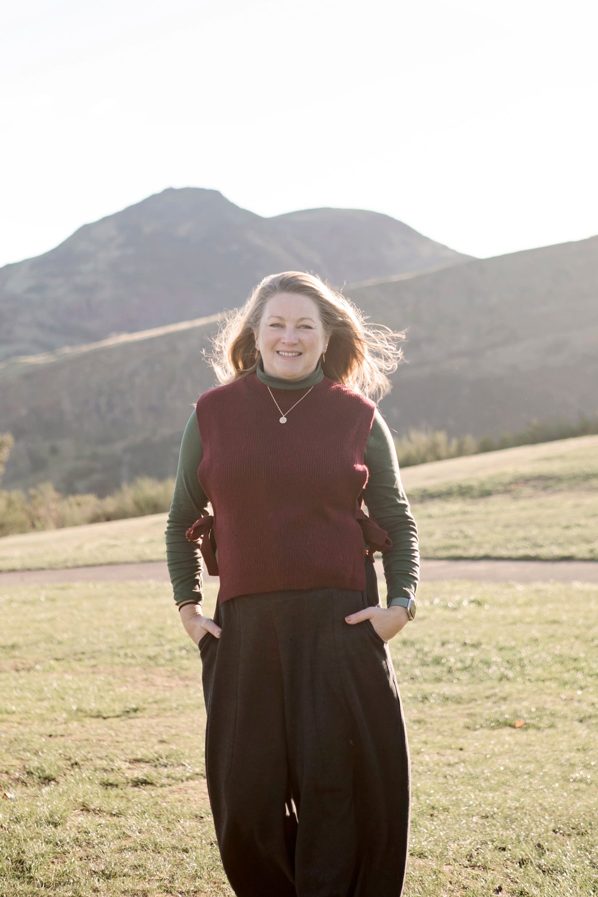 Woman (Helen of HR Digital Design) standing in a field with Arthurs Seat in Edinburgh and the Crags in the background