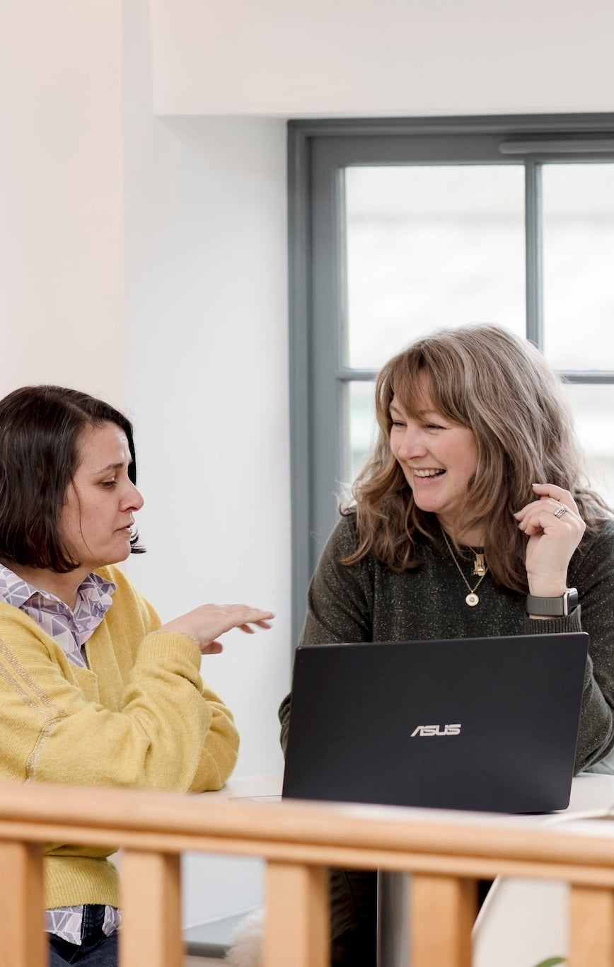 Two women sitting at a table with an ASUS laptop, engaged in a conversation.